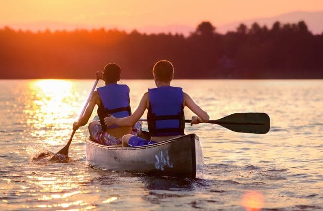 two boys paddling a canoe into the sunset