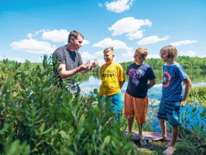 counselor showing three boys two different flowers in front of the lake