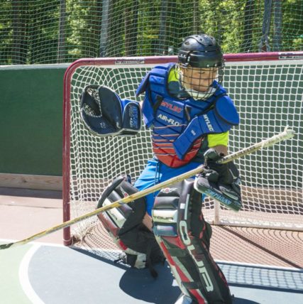 boy in hockey goalie padding in front of a goal