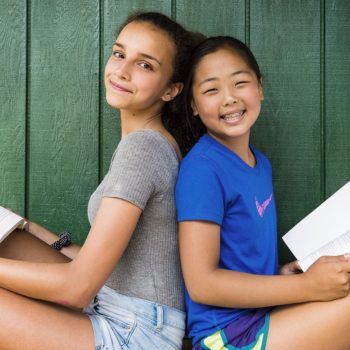 two girls sitting back to back holding books