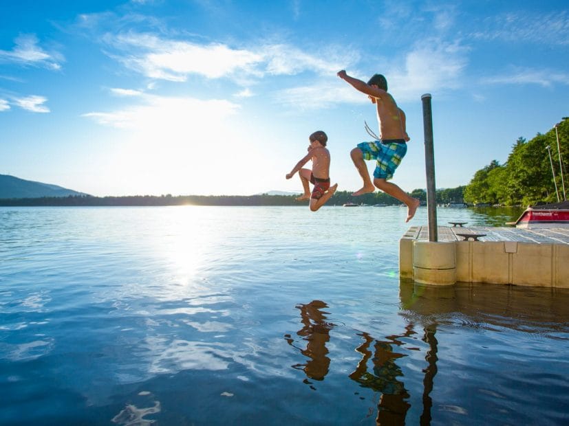 two boys jumping in a lake as the sun's reflection bounces off the water