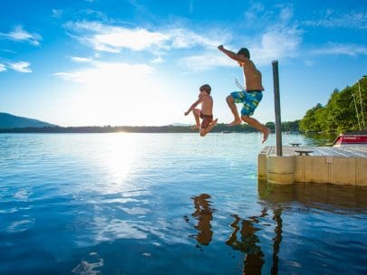 two boys jumping off a pier into a lake