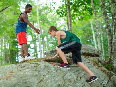 boy climbing a rock while another offers a helping hand