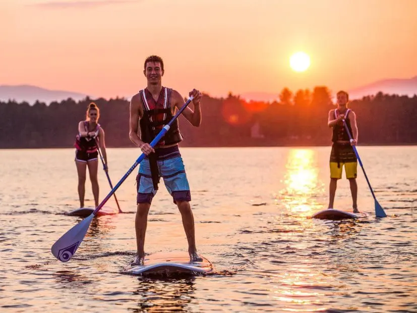 three campers on standing paddle boats at sunset