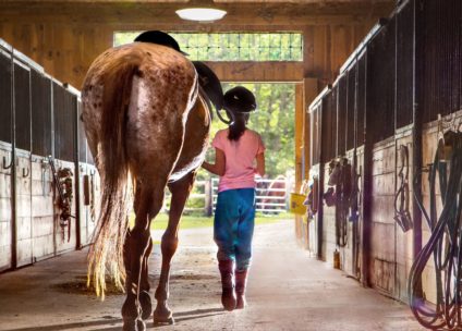 young girl and a horse walking through a stable