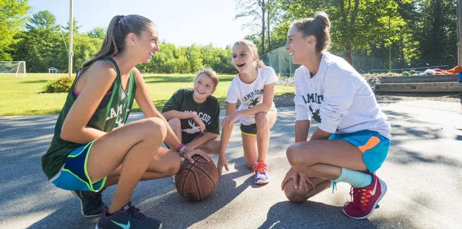 two counselors and two campers kneeling on the basketball court