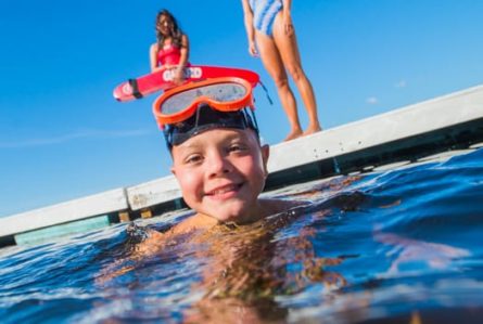 boy with scuba goggles in the water while a lifeguard watches
