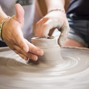 two right hands working to form a ceramic pot