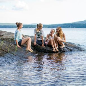 four girls on a rock next to the lake