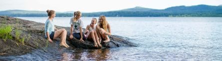four girls sitting on a rock jutting out of a lake