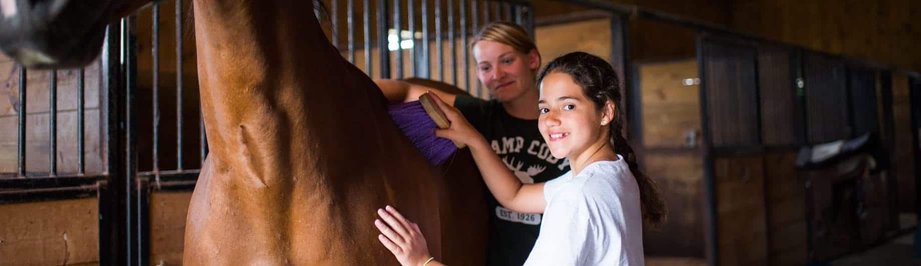girl camper brushing a horse while a counselor watches