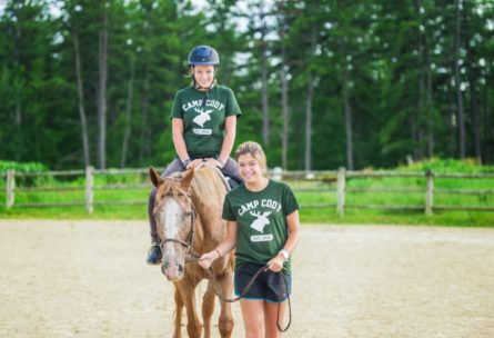 an instructor leading a camper who's on a horse