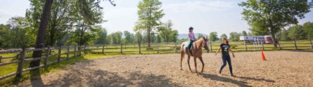 young girl rides a horse while an instructor leads them