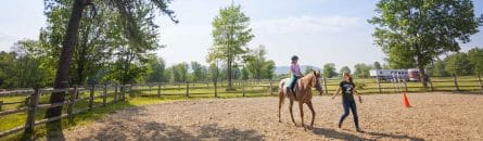 a camper riding a horse while an instructor leads them