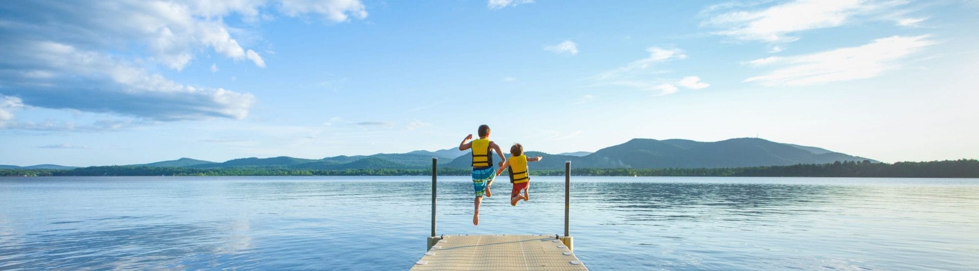 two boys jumping off a pier into a lake