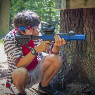 boy squatting while shooting a paintball gun