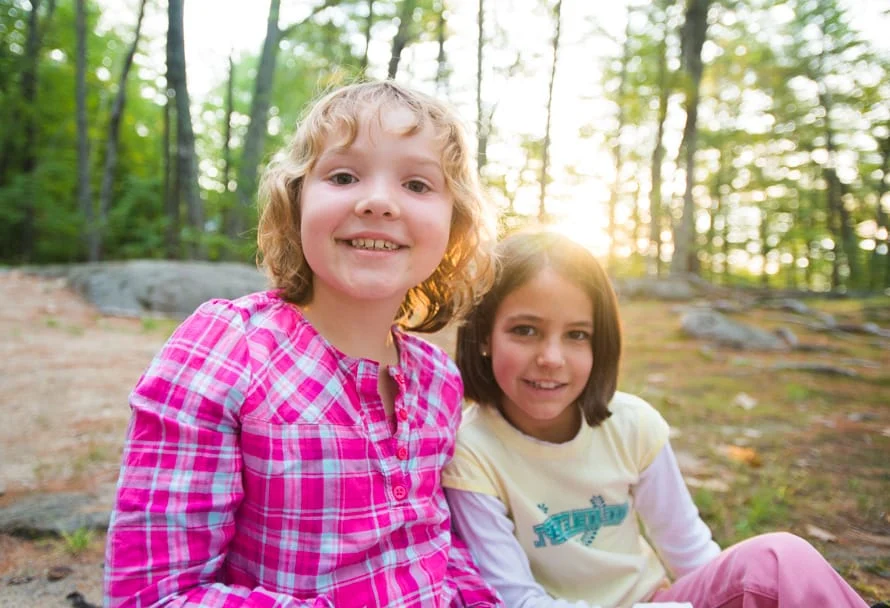 two young campers in the woods with the sun peaking through the trees behind them