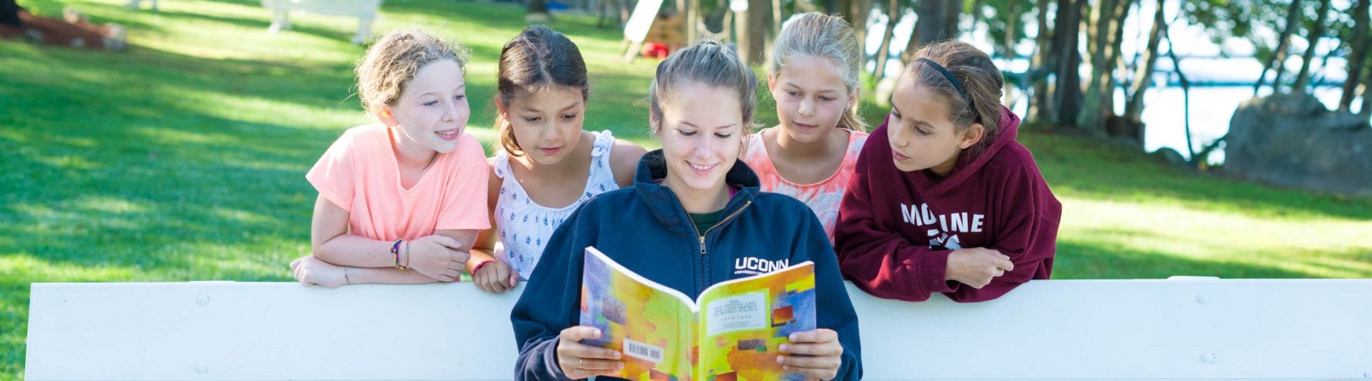 girl counselor reading while four young girls look over her shoulder