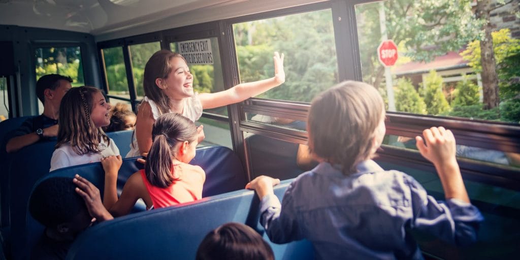 kids smiling while looking outside bus window