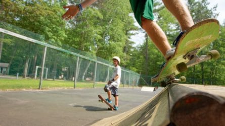 close up of a skateboard grind while another camper watches