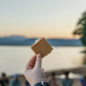 holding a smore in front of a lake at sunset.