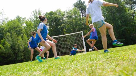 soccer goalie diving for the ball in front of a net while other campers on the same team watch