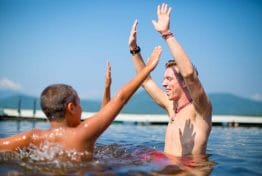 counselor with raised hands while in the lake with two boys