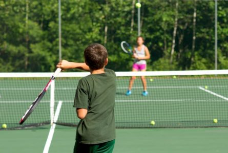 boy hitting a tennis ball over the net to a girl