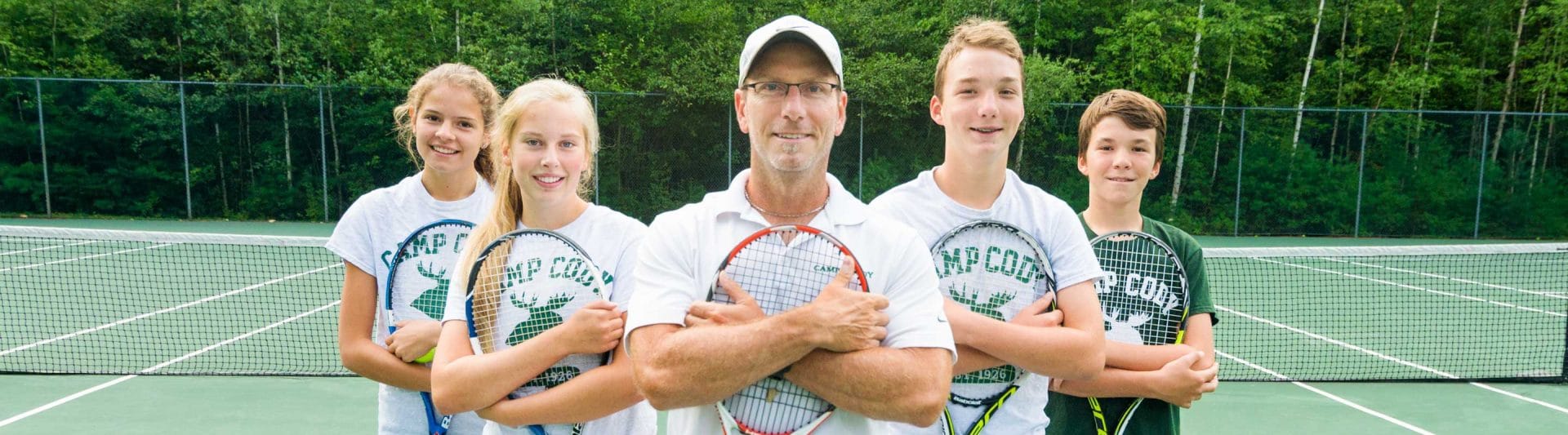 tennis coach and four players flanking him hugging their tennis rackets to their chests