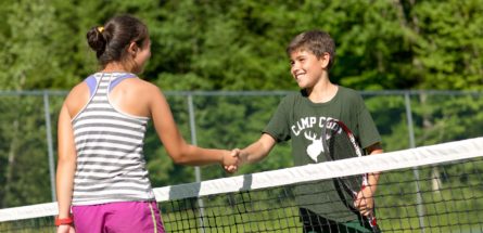 a boy and girl shaking hands over a tennis net