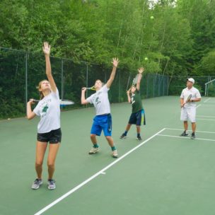 campers practice their serving technique while a coach watches them