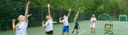 our campers practicing their tennis serve while a coach watches