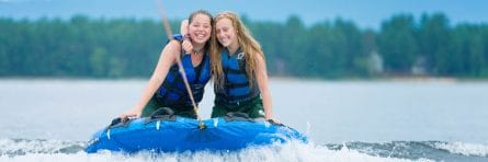 two girls smiling while riding an inflatable being pulled by a rope
