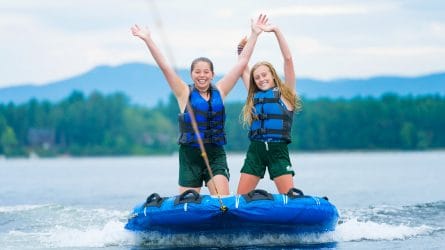 girls raising their hands while riding a water board