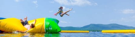 a guy launching a young girl off of an inflatable into the air on a lake