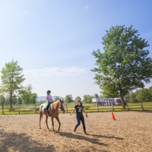 young girl riding a horse while an instructor leads them
