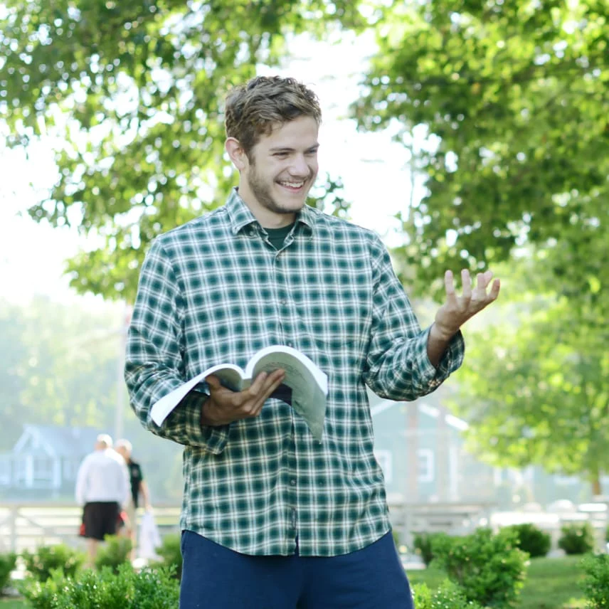 a young man smiling while reading a book