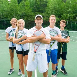 tennis instructor with students, hugging tennis rackets