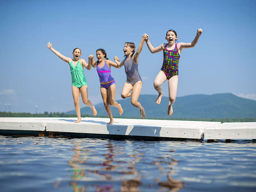 four girls holding hands and jumping into lake