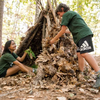 boy and girl making a natural shelter in the woods.